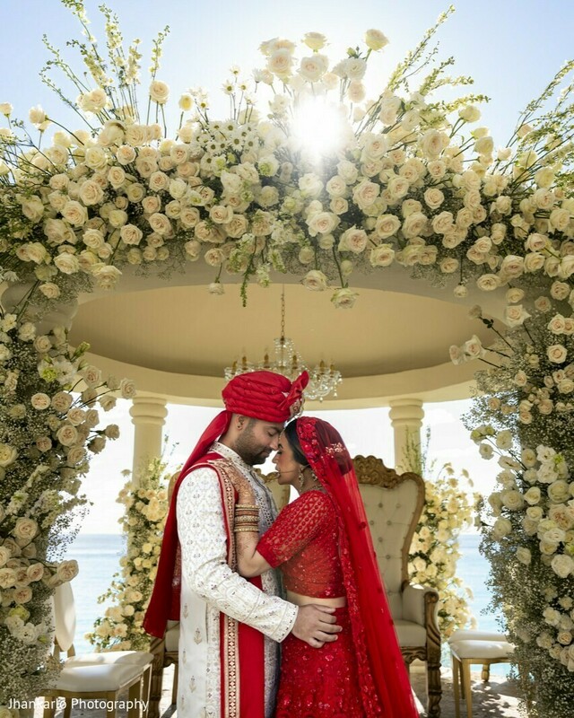 groom portrait,red sherwani,floral mandap,ocean view,cancun wedding,wedding ceremony,majestic moment,cultural attire,destination vows,sunlight backdrop