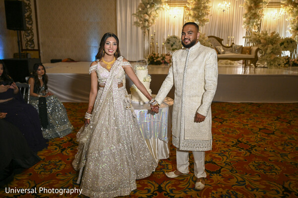 reception couple portrait,indian bride and groom,elegant backdrop,glamorous wedding,wedding photography,reception attire,couple holding hands,timeless portrait,golden decor,wedding elegance