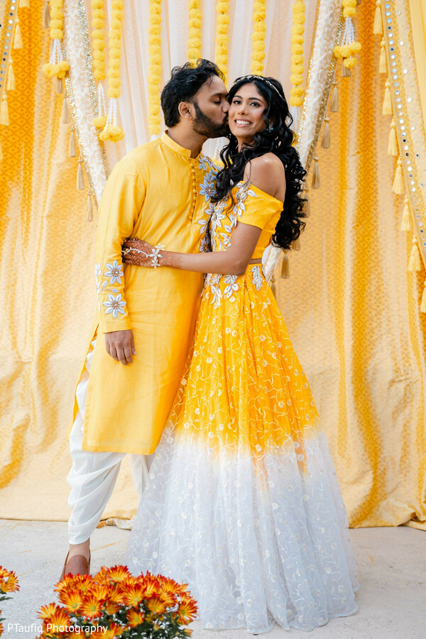 haldi couple portrait,yellow haldi outfits,floral embroidery,bride and groom kiss,indian pre-wedding event,marigold backdrop,traditional haldi ceremony,joyful wedding moment,south asian wedding style,pastel yellow decor