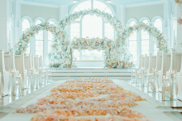 indoor ceremony,floral arch,white decor,luxury venue,wedding aisle,pastel palette,romantic altar,elegant design,timeless ceremony,fairy tale wedding