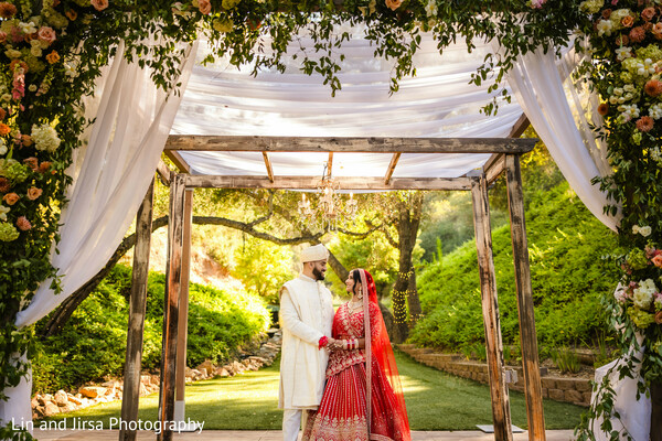 couple portrait,garden bridge,romantic gaze,red bridal lehenga,ivory sherwani,outdoor wedding,south asian couple,post-ceremony shoot,serene love,natural beauty