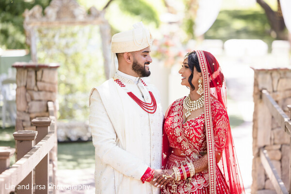 couple portrait,red bridal lehenga,ivory sherwani,romantic gaze,outdoor wedding,garden bridge,south asian couple,hindu wedding,elegant attire,love moment