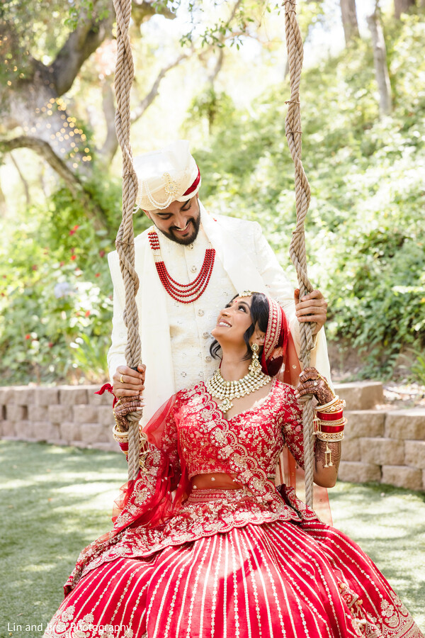 couple portrait,wedding swing,outdoor greenery,red bridal lehenga,ivory sherwani,romantic pose,playful love,south asian couple,garden backdrop,candid joy