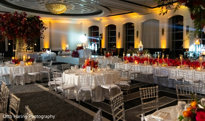 reception decor,ballroom lighting,red floral centerpieces,luxury wedding,indoor venue,elegant tablescape,romantic lighting,gold accents,south asian reception,candlelight