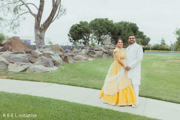 pre-wedding portrait,yellow lehenga,white sherwani,outdoor setting,joyful couple,bright colors,south asian engagement,cultural attire,natural background,elegant pose