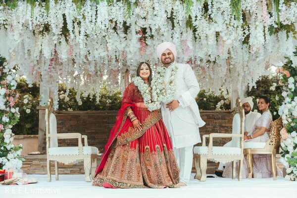 hindu ceremony,mandap decor,garland exchange,joyful couple,wedding rituals,red bridal lehenga,ivory sherwani,candid moment,outdoor ceremony,south asian traditions