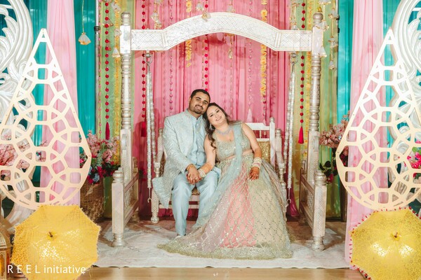 mehndi decor,pastel mandap,couple portrait,joyful bride,pre-wedding celebration,floral backdrop,colorful drapes,south asian couple,henna day,cultural festivity