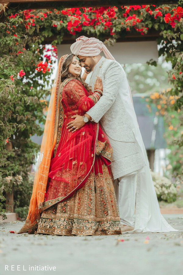 bridal lehenga red,ivory sherwani,couple embrace,floral arch,outdoor portrait,romantic moment,south asian wedding,gold embroidery,newlyweds,garden backdrop