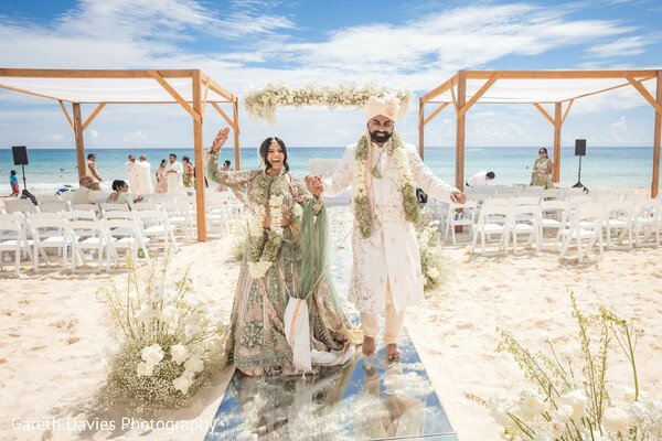 south asian newlyweds,wedding exit moment,beach wedding celebration,floral petal toss,joyful wedding walk,destination wedding joy,hindu wedding couple,post-ceremony bliss,seaside wedding aisle,just married moment