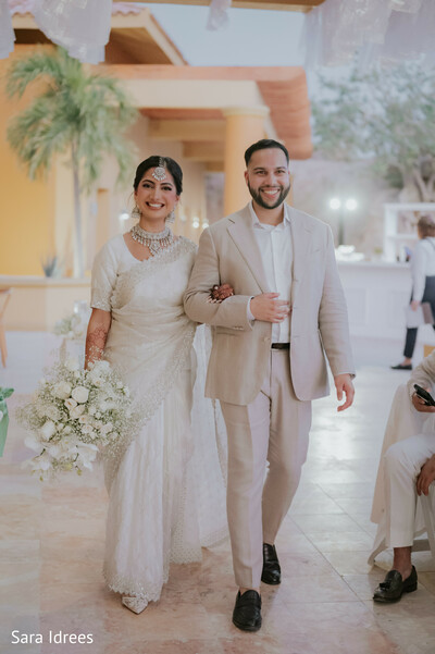 wedding recessional,indian bride walking,groom in beige suit,joyful wedding moment,destination wedding venue,ivory wedding look,modern south asian wedding,post ceremony smiles,elegant couple walk,celebratory atmosphere