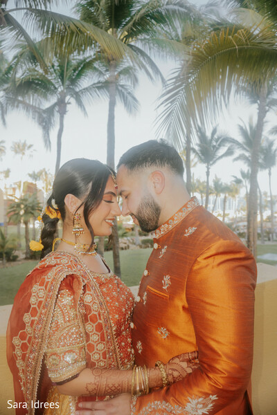 destination wedding portraits,palm tree wedding,golden hour couple,rust bridal lehenga,groom in embroidered sherwani,romantic forehead touch,tropical indian wedding,intimate wedding moment,sunset romance,destination love story
