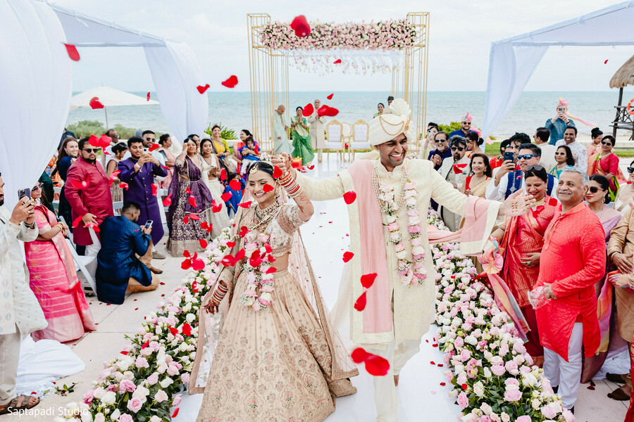 destination indian wedding,beach wedding ceremony,rose petal toss,bride and groom exit,wedding aisle decor,joyful celebration,oceanfront mandap,south asian wedding rituals,festive crowd,unforgettable moment