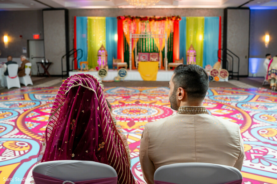 wedding ceremony seating,south asian rituals,mandap decor,couple candid,pre ceremony moment,traditional wedding stage,cultural wedding setup,intimate wedding pause,ceremonial details,wedding symbolism