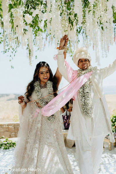 wedding recessional,floral mandap,ivory wedding attire,jaimala garlands,hindu wedding ceremony,newlyweds celebration,raised hands moment,sacred vows,outdoor ceremony,marital joy