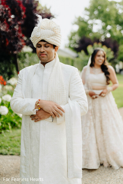 first look moment,groom portrait,ivory sherwani,bridal approach,wedding anticipation,emotional wedding moment,outdoor ceremony,traditional groom attire,love unfolding,quiet romance