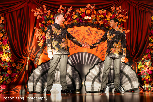 lgbtq south asian couple,wedding performance stage,luxury reception decor,embroidered sherwani looks,joyful celebration,floral stage backdrop,cultural fusion wedding,dramatic lighting,modern indian wedding