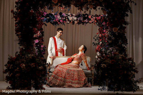 mandap lounge,floral wedding decor,romantic couple portrait,indian wedding mandap,dramatic wedding lighting,red bridal lehenga,groom sherwani,luxury wedding design,seated bride portrait,south asian wedding style