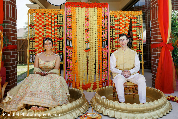 haldi ceremony,marigold decor,seated haldi ritual,pastel indian outfits,pre wedding ceremony,floral backdrop,cultural traditions,joyful couple,outdoor indian wedding,ceremonial seating