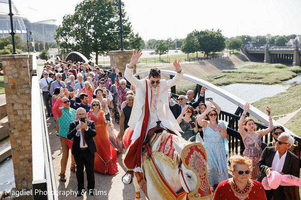baraat procession,groom on horseback,indian wedding baraat,wedding celebration crowd,traditional groom attire,red stole groom,joyful wedding moment,outdoor baraat,wedding guests cheering,south asian wedding ritual