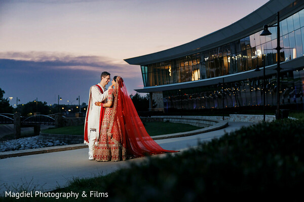 blue hour wedding portrait,architectural wedding venue,red bridal veil train,outdoor couple portrait,modern wedding aesthetic,twilight wedding photo,indian wedding fashion,elegant bride groom,romantic evening portrait,luxury wedding