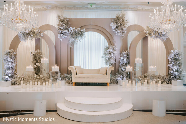 luxury reception stage,ivory wedding decor,floral wedding backdrop,crystal chandeliers,candlelit wedding stage,elegant indian reception,grand ballroom wedding,white floral design,wedding lounge setup,sophisticated wedding styling