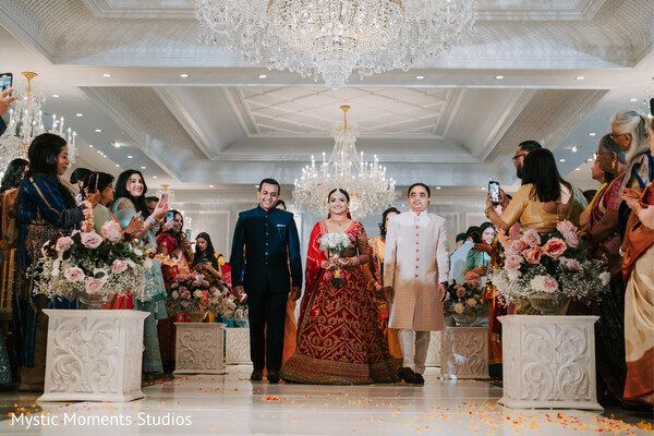 bridal entrance,red bridal lehenga,gold embroidery lehenga,chandelier wedding venue,aisle floral decor,hindu wedding ceremony,luxury indian wedding,bride walking down aisle,traditional bridal look,grand wedding entrance