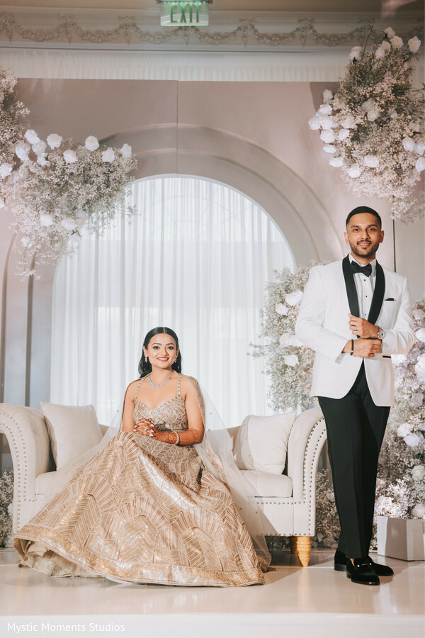 reception couple portrait,champagne bridal lehenga,white tuxedo groom,elegant wedding stage,floral arch decor,luxury indian reception,formal wedding attire,sophisticated wedding styling,ballroom wedding portrait,romantic couple pose