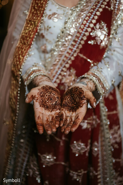 bridal mehndi design,circular henna pattern,red and ivory lehenga details,henna ceremony,traditional south asian ritual,intricate hand art,bridal bangles,cultural wedding detail,wedding day close-up,mehndi symbolism