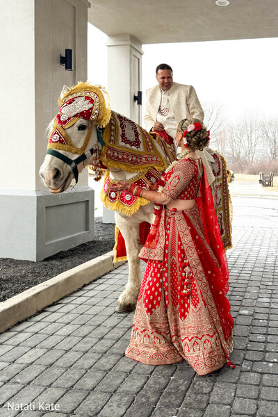 baraat horse,traditional groom entrance,ivory sherwani groom,red bridal lehenga,decorated wedding horse,south asian wedding ritual,ornate horse embroidery,cultural procession moment,outdoor wedding arrival,festive wedding tradition