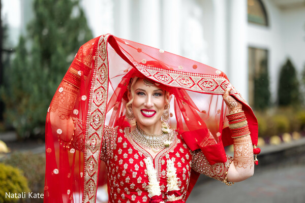 red bridal dupatta,bridal mehndi hands,gold bridal jewelry,embroidered lehenga detail,smiling bride portrait,hindu wedding fashion,chooda bangles,bridal veil moment,cultural bridal elegance,outdoor wedding portrait