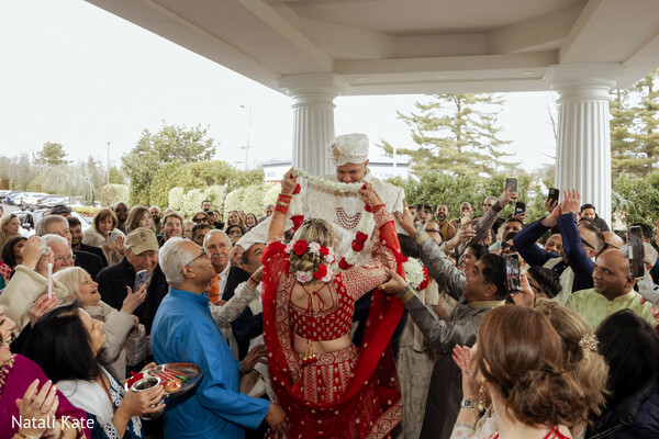 varmala ceremony,garland exchange ritual,playful wedding tradition,cheering wedding guests,red bridal lehenga,ivory sherwani groom,hindu wedding ceremony,family celebration moment,joyful cultural ritual,wedding crowd energy