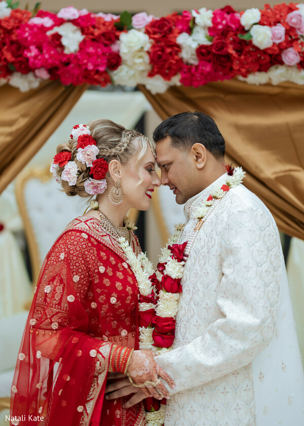 red bridal lehenga,ivory sherwani,floral mandap canopy,varmala garlands,hindu wedding ceremony,forehead touch pose,gold bridal jewelry,embroidered dupatta,romantic mandap portrait,sacred wedding ritual