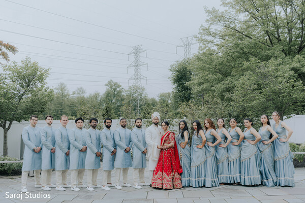 bridal party portrait,bridesmaids in blue lehengas,groomsmen in pastel kurtas,coordinated wedding colors,red bridal lehenga centerpiece,outdoor wedding group shot,hindu wedding celebration,modern bridal squad,cultural wedding fashion,symmetrical wedding lineup