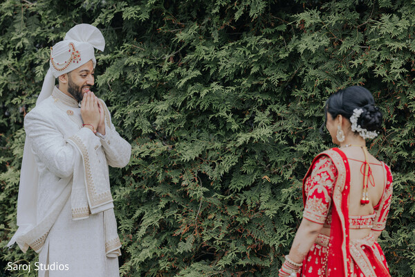 first look moment,groom namaste gesture,red bridal lehenga,emotional wedding reaction,ivory sherwani groom,hindu wedding tradition,outdoor garden setting,romantic reveal,cultural wedding ritual,intimate couple exchange