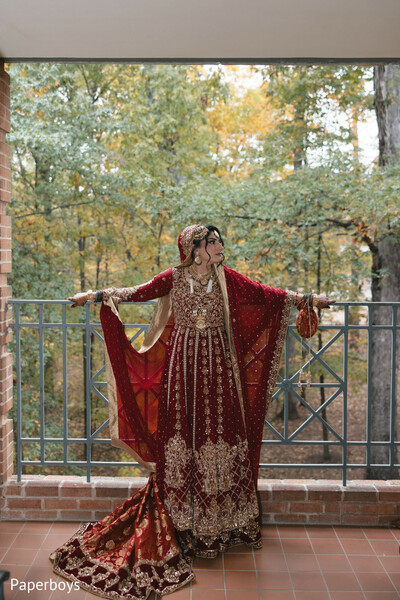 balcony bridal portrait,red dupatta drape,gold embroidered lehenga,autumn wedding backdrop,regal bridal stance,flowing bridal train,south asian wedding fashion,outdoor bridal elegance,traditional wedding attire,dramatic bridal pose