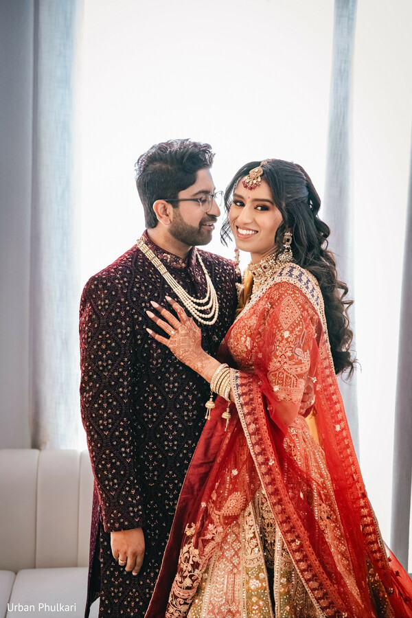 red bridal lehenga,maroon sherwani groom,pearl layered necklace,romantic couple portrait,south asian bridal jewelry,embroidered wedding outfit,intimate wedding moment,luxury indian wedding fashion,bride smiling portrait,classic wedding