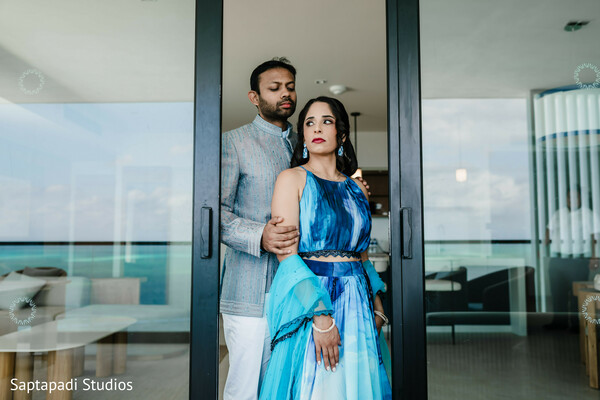 blue bridal lehenga,ocean view portrait,destination wedding photography,modern south asian couple,seaside wedding location,elegant couple portrait,contemporary indian fashion,romantic wedding moment,coastal luxury wedding,glass doorway portrait