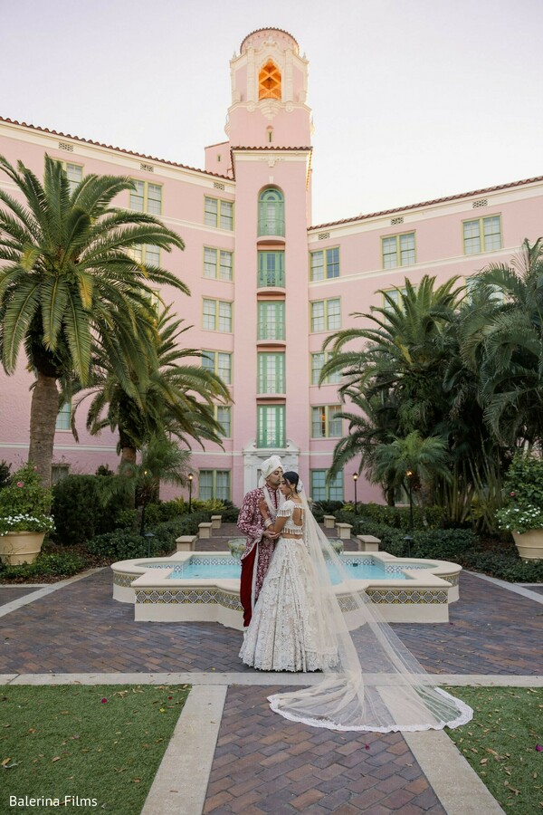 destination wedding couple portrait,pastel pink resort venue,ivory bridal lehenga,groom sherwani attire,romantic fountain portrait,luxury indian destination wedding,south asian bride and groom,elegant wedding veil train,palm tree wedding backdrop,timeless wedding photography