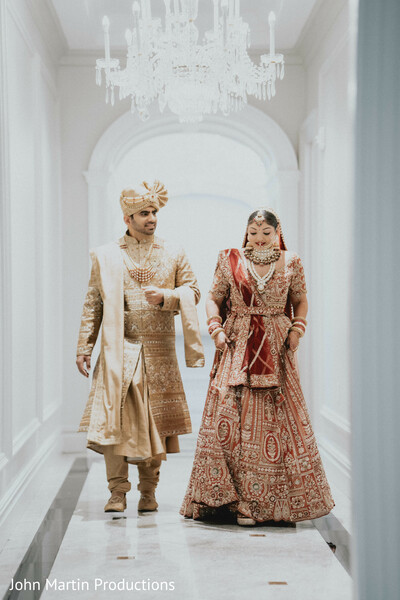bride and groom walking,indian wedding couple portrait,bridal lehenga red,groom sherwani gold,luxury wedding venue hallway,elegant wedding photography,south asian wedding style,traditional wedding attire,romantic couple moment,classic wedding portrait