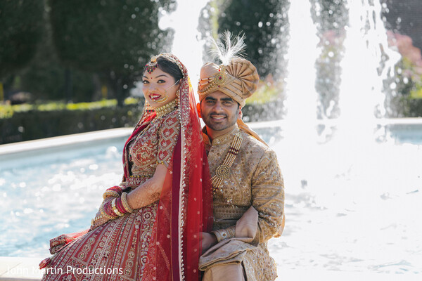bride and groom fountain portrait,romantic wedding couple,indian wedding attire,red bridal lehenga,groom sherwani outfit,outdoor wedding photography,luxury wedding portrait,south asian wedding couple,elegant couple pose,destination wedding moment