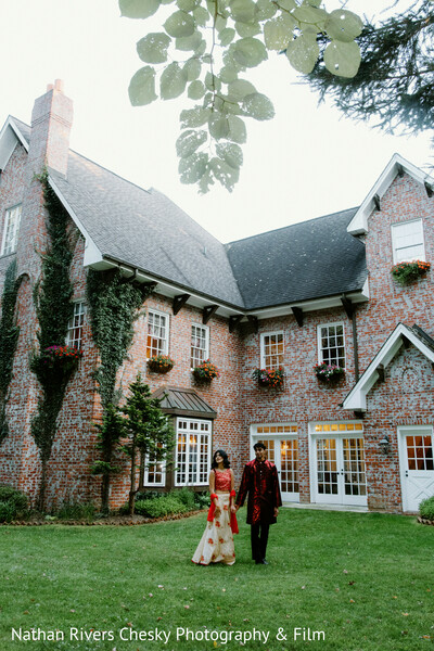estate wedding venue,couple walking hand in hand,outdoor wedding portrait,brick mansion backdrop,garden wedding,indian couple pre wedding,romantic stroll,south asian wedding photography,scenic venue,nature wedding
