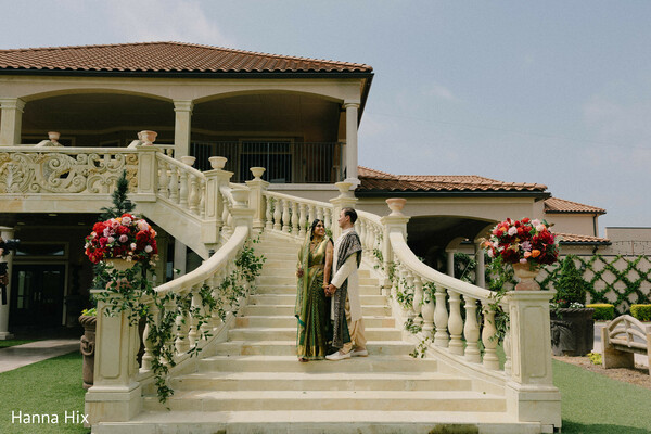 indian wedding couple,green bridal saree,ivory sherwani groom,grand staircase decor,floral aisle arrangements,romantic couple portrait,luxury wedding venue,outdoor wedding setting,elegant indian attire,wedding architecture backdrop