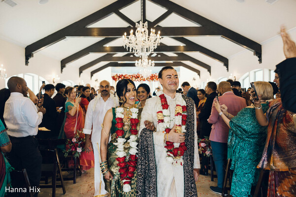 wedding aisle walk,just married couple,floral aisle decor,wedding guests cheering,hindu wedding exit,couple smiling moment,celebration atmosphere,indoor wedding ceremony,bride groom garlands,joyful wedding moment