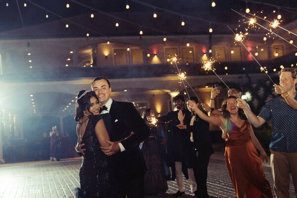 wedding sparkler exit,nighttime wedding celebration,romantic couple moment,wedding reception night,guests with sparklers,bride groom embrace,evening wedding vibes,joyful celebration moment,wedding send off,romantic night portrait