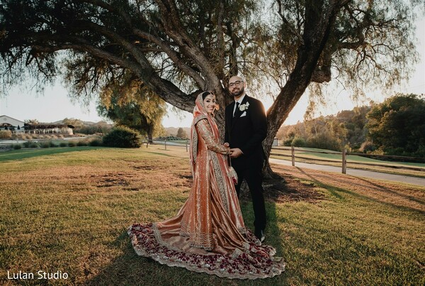 golden hour couple portrait,outdoor wedding nature,bride lehenga train,groom tuxedo,romantic sunset shot,natural wedding backdrop,scenic couple portrait,wedding photography outdoors,soft light romance,countryside wedding