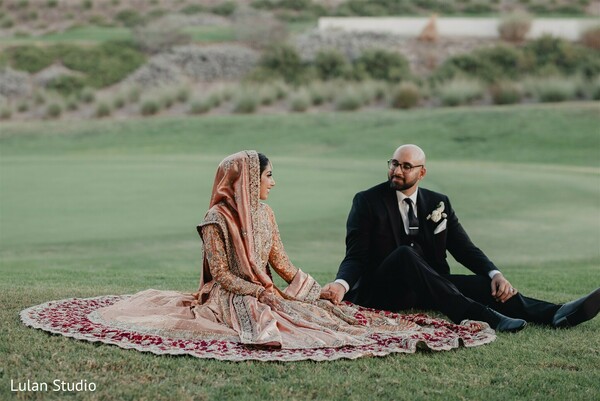 couple sitting on grass,outdoor wedding portrait,bride lehenga details,groom tuxedo,relaxed wedding moment,romantic candid couple,scenic wedding location,intimate portrait,natural light wedding,couple connection