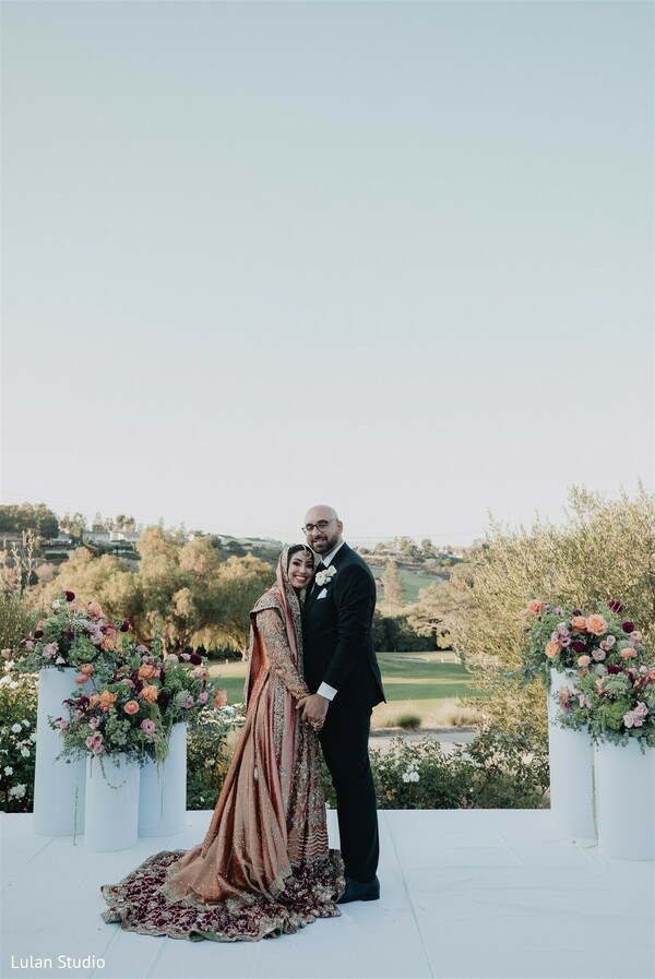 outdoor wedding ceremony,floral altar decor,couple portrait ceremony,scenic wedding view,pastel floral arrangements,bride groom standing,elegant wedding setup,romantic outdoor wedding,ceremony backdrop,wedding florals