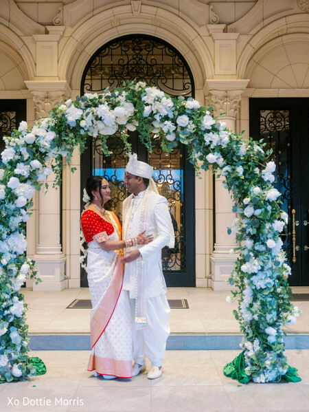 floral arch wedding,outdoor ceremony decor,couple under arch,romantic wedding portrait,greenery backdrop,bride groom intimate,elegant ceremony setup,floral installation,wedding couple,dreamy decor
