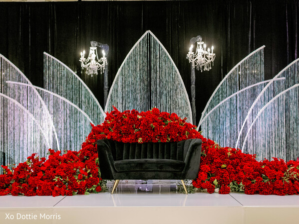 reception stage decor,red rose backdrop,luxury wedding stage,modern indian decor,chandelier lighting,floral installation,dramatic wedding design,elegant stage setup,wedding decor inspiration,statement backdrop