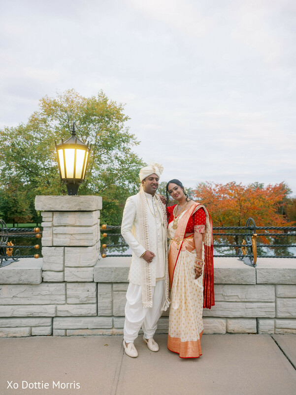 outdoor couple portrait,fall wedding colors,bride saree red white,groom sherwani,scenic wedding backdrop,romantic outdoor setting,natural light portrait,couple standing,autumn wedding,elegant couple